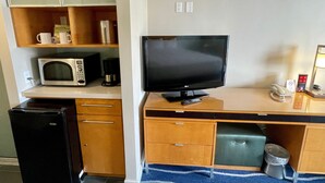 A compact kitchenette with a microwave, coffee maker, and a small refrigerator. A flat-screen TV is mounted on a wooden cabinet, and a trash bin is visible. - Last Minute Spacial! Oceanview's on 31st Flr (Honolulu)
