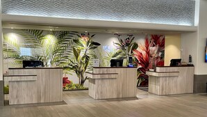 A reception area with three wooden reception desks, a bench, and a wall decorated with tropical plants. - Last Minute Spacial! Oceanview's on 31st Flr (Honolulu)