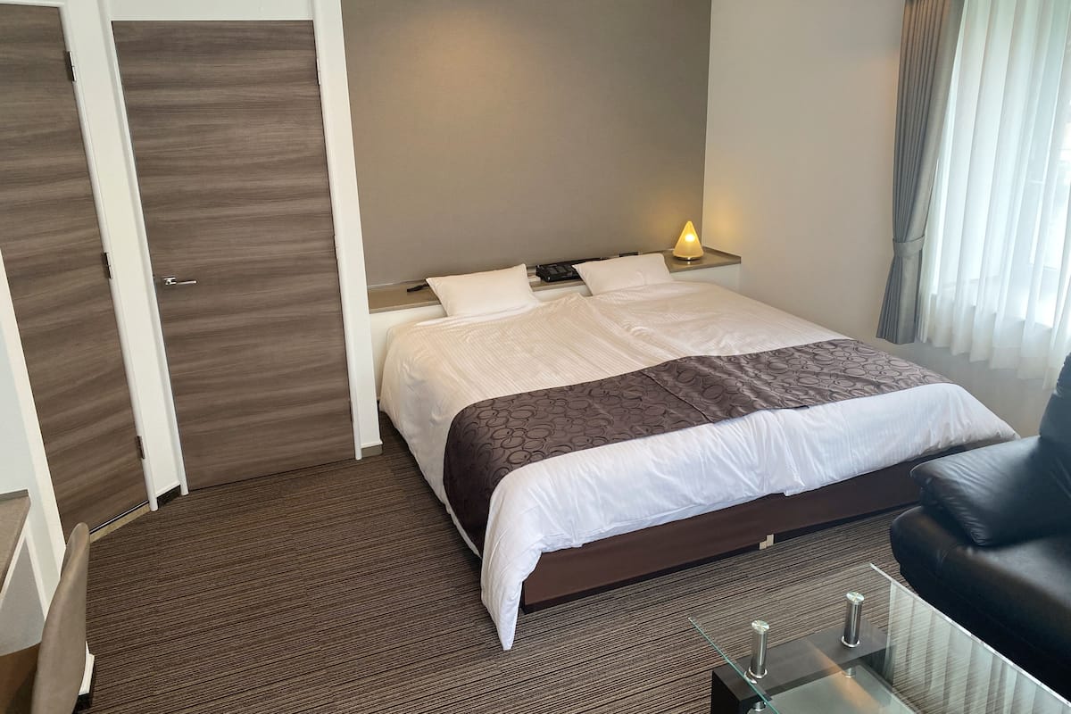 A hotel room with a bed, a nightstand with a lamp, a leather armchair, and a glass coffee table.