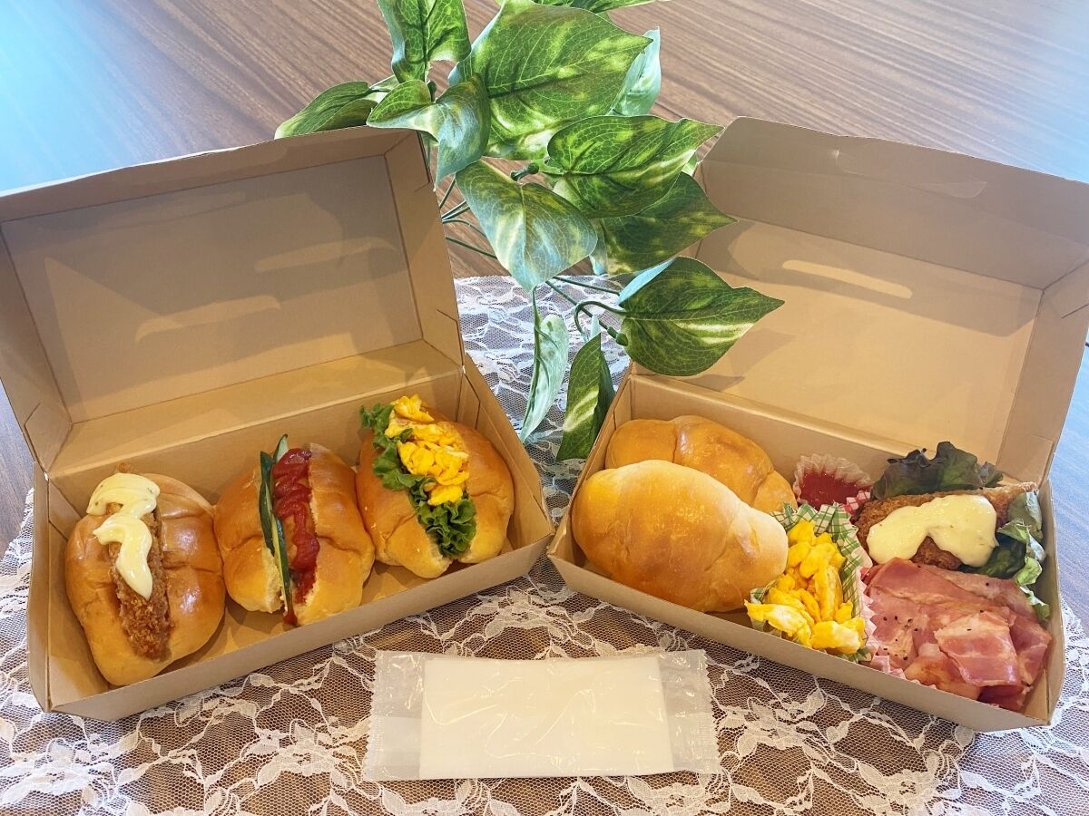 Two open food boxes on a lace tablecloth with a plant in the background.