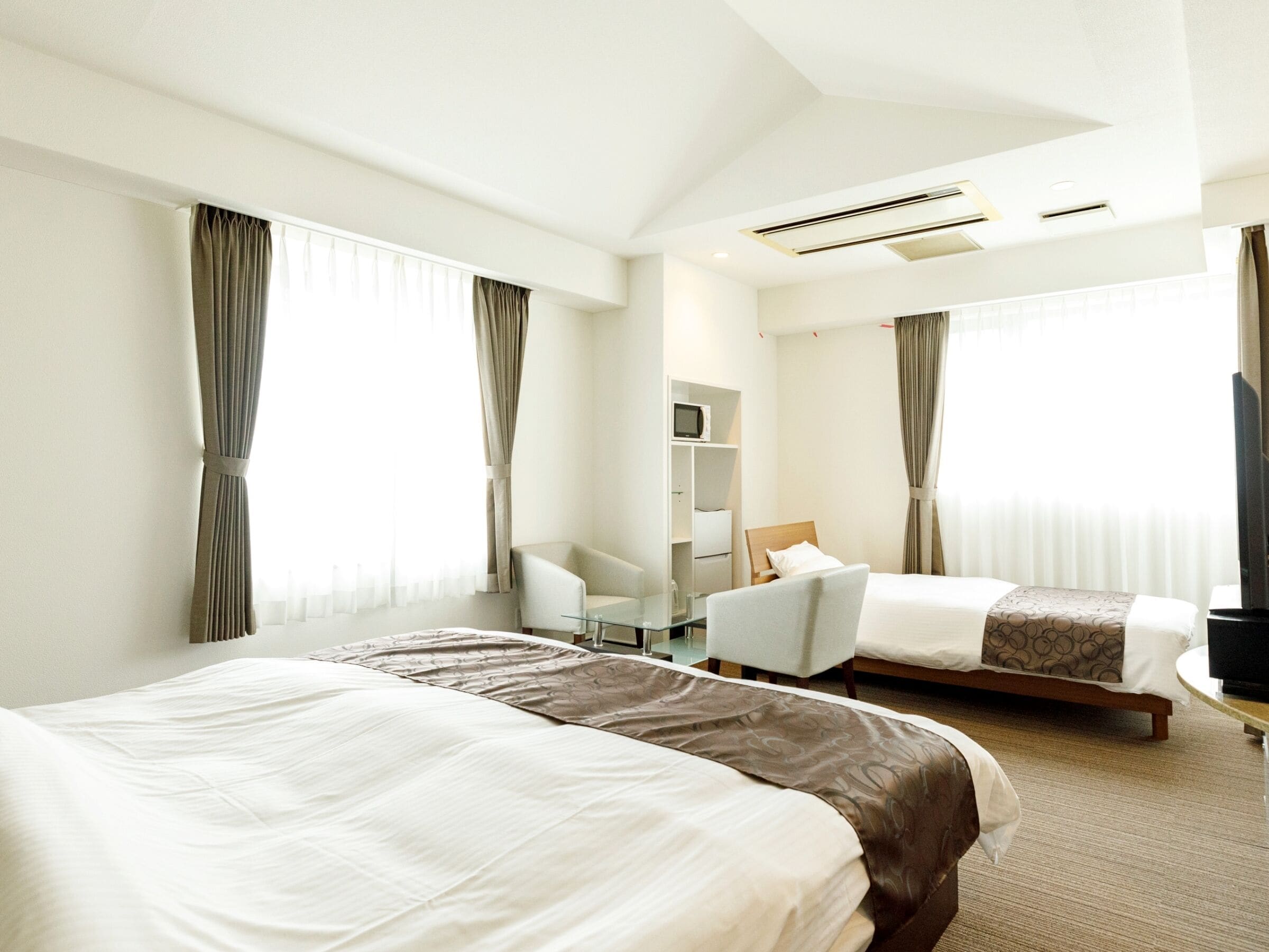A hotel room with two beds, a desk, a chair, and a TV.