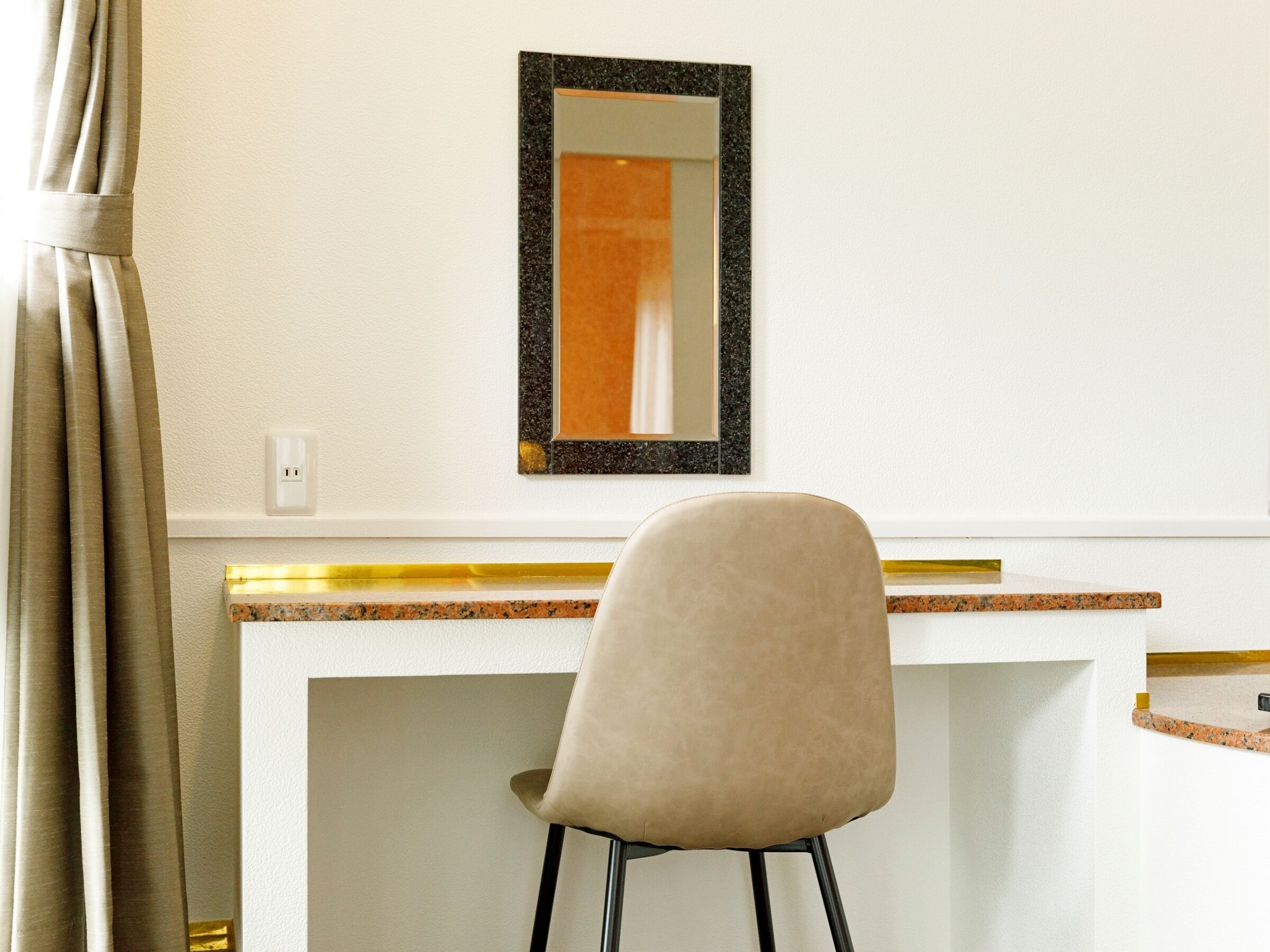 A hotel room with a desk, chair, and a mirror.