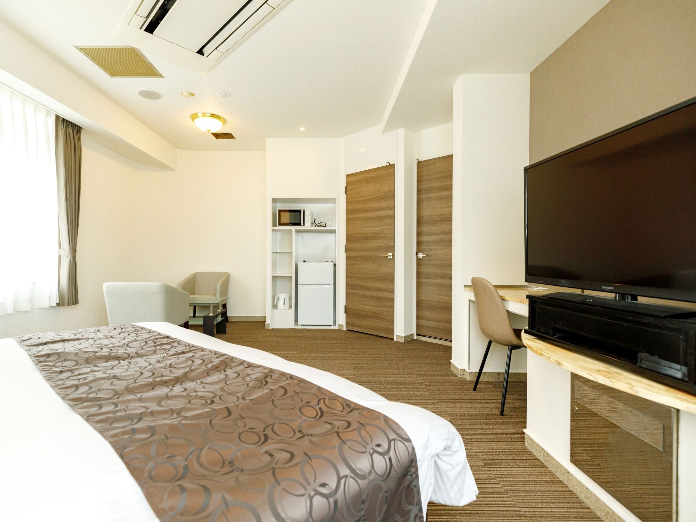 Habitación de hotel con una cama grande, un escritorio con televisor de pantalla plana, una silla, minibar y armario.