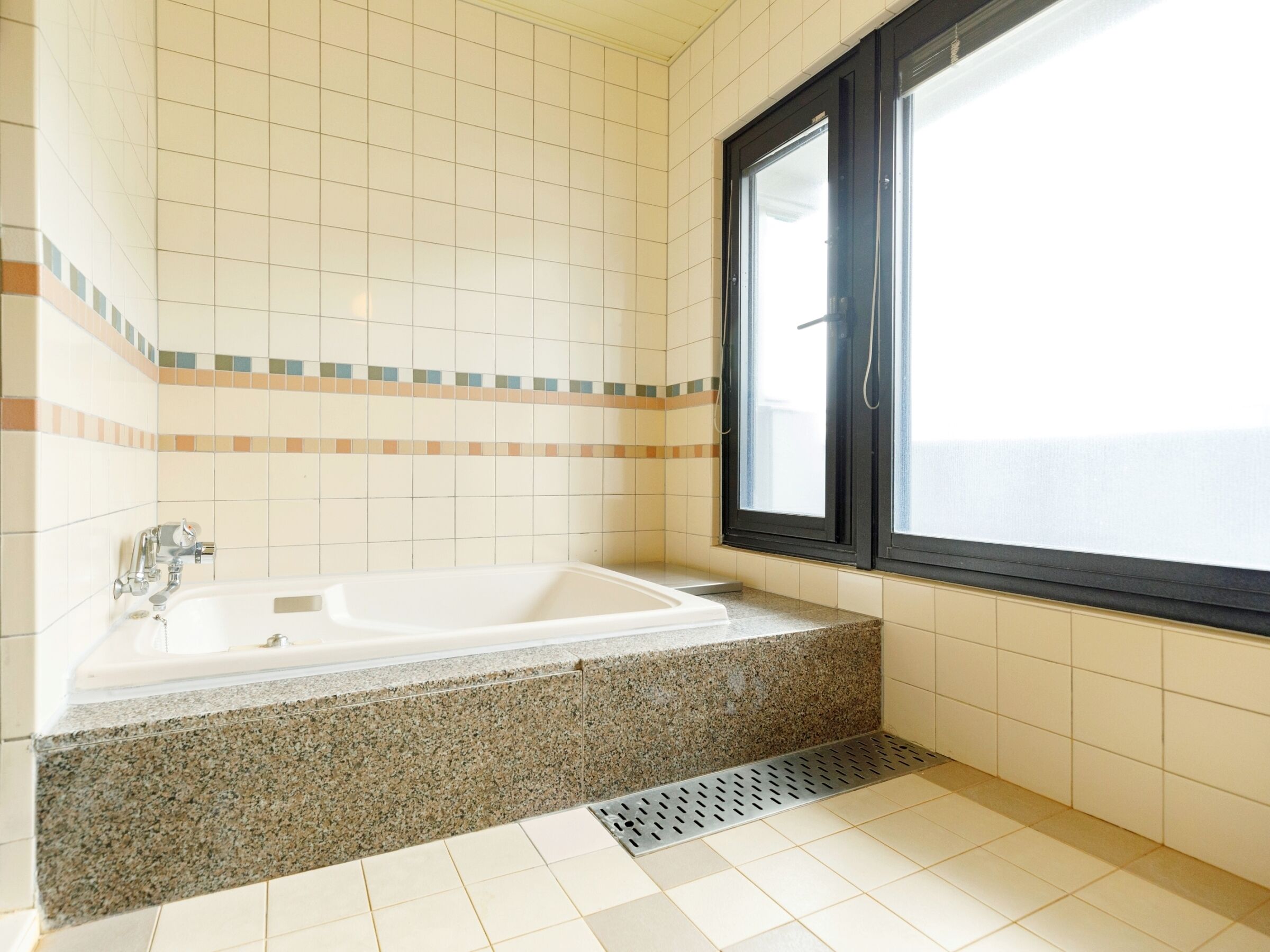 A bathroom with a bathtub, a window, and tiled walls.