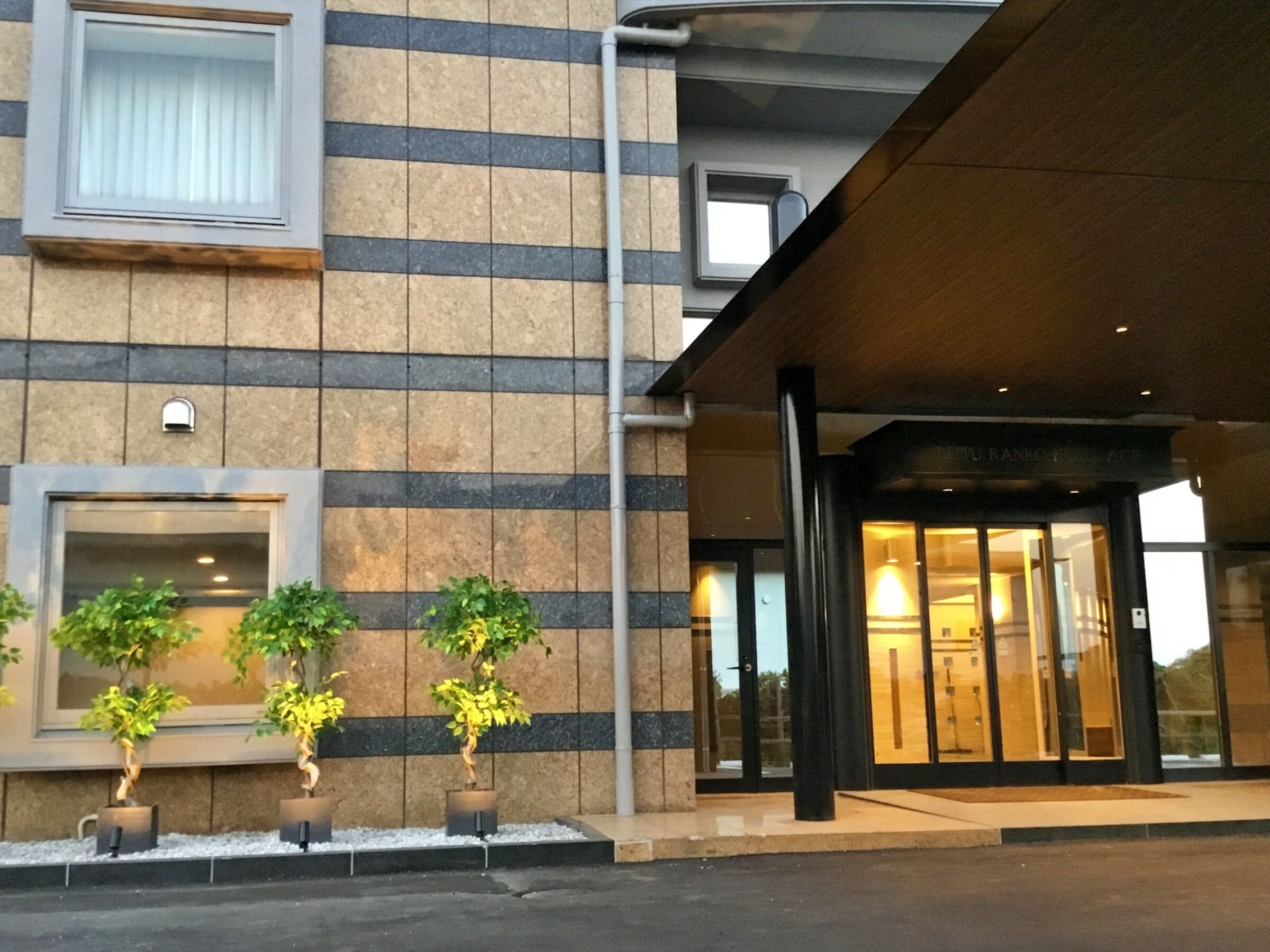 A hotel entrance with a modern design, featuring a stone facade, a glass door entrance, and potted plants.