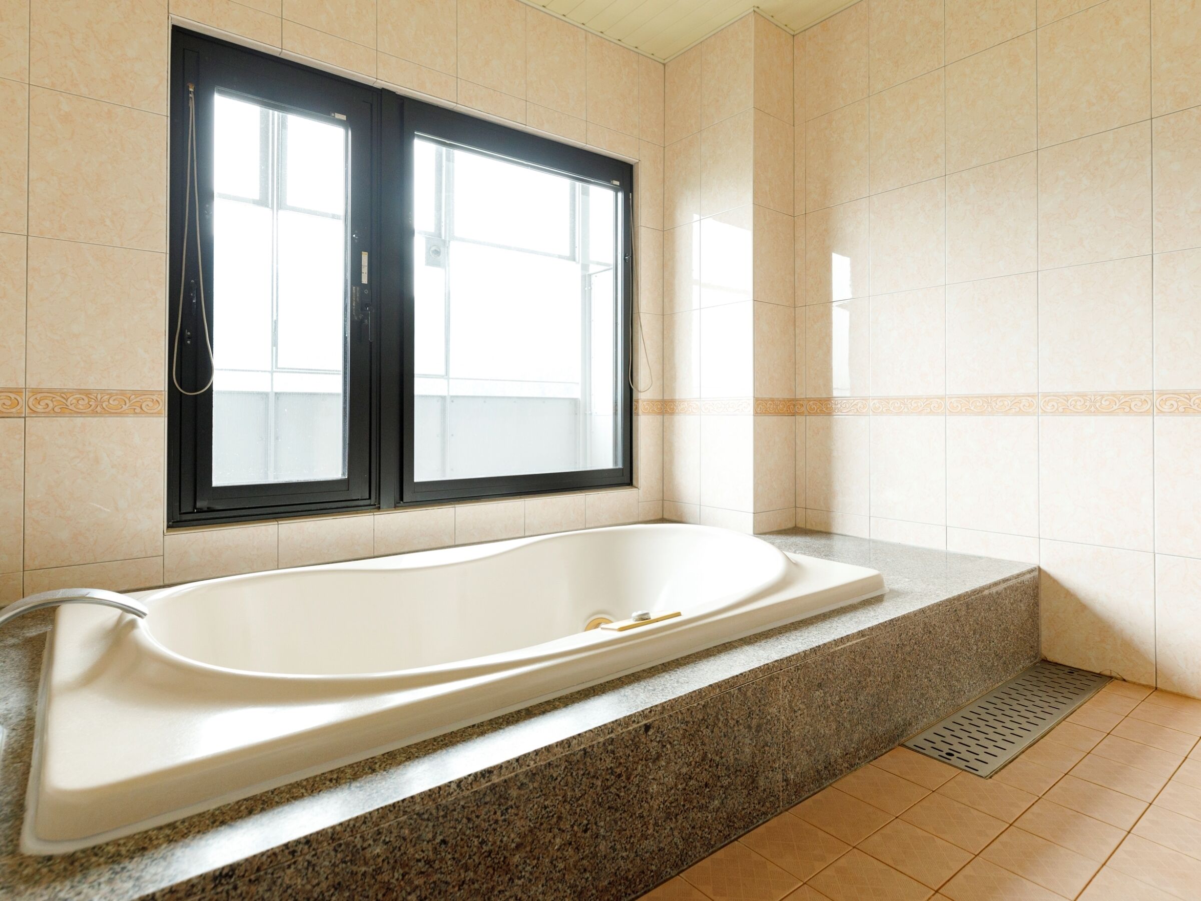 A bathroom with a large bathtub, a window, and tiled walls.