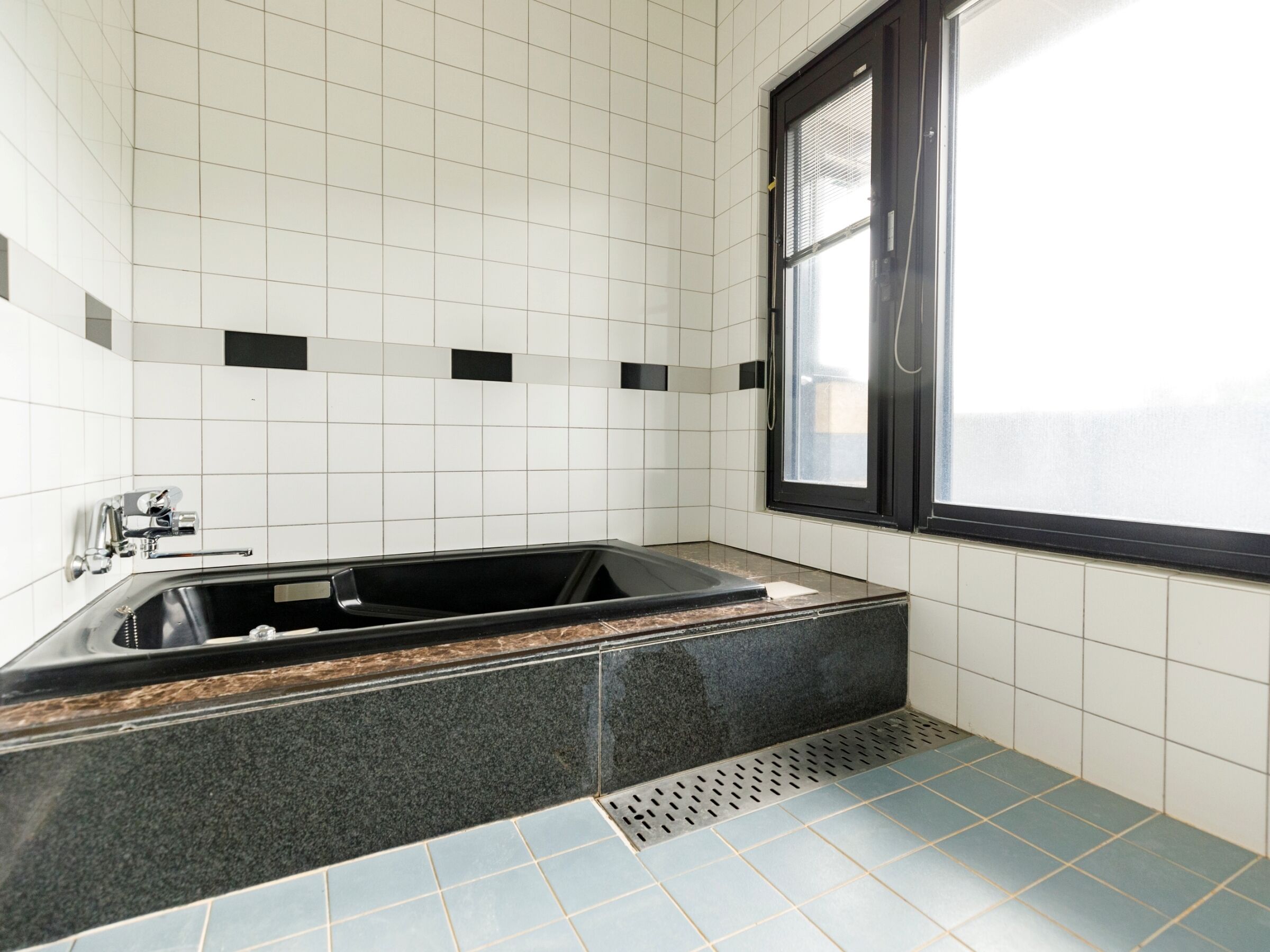 Un bagno moderno con una vasca da bagno nera, pareti rivestite di piastrelle bianche e una finestra con persiane.