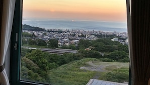 A view from a window overlooking a cityscape with a body of water in the distance, greenery in the foreground, and a clear sky. - BEPPU KANKO HOTEL ACE (Beppu)