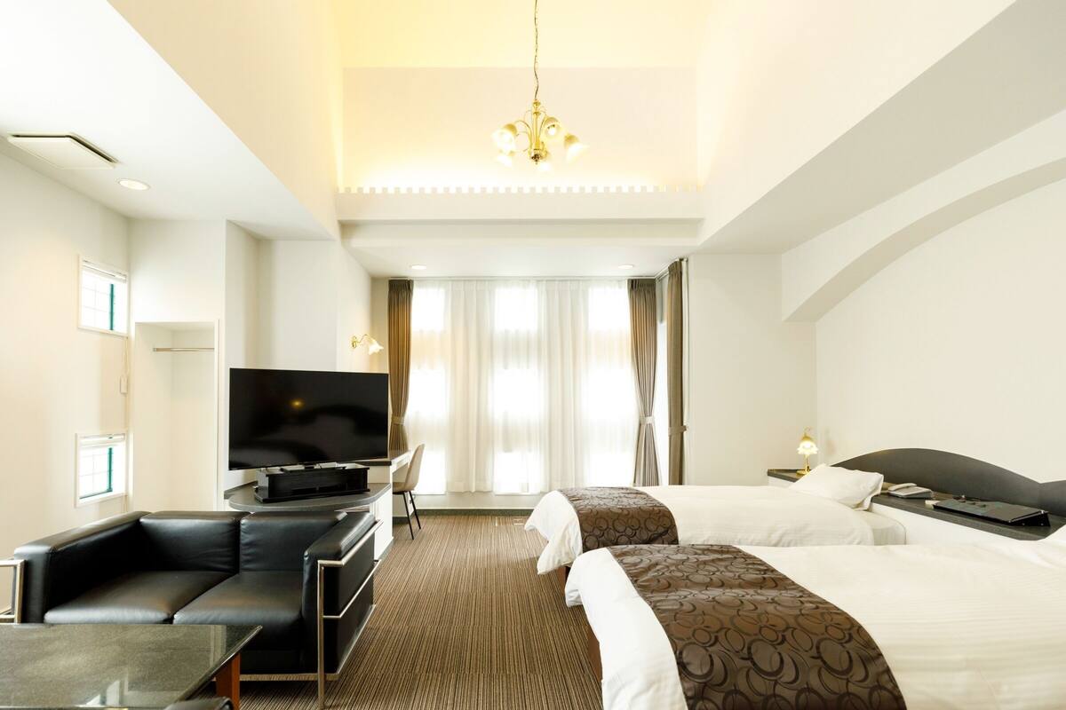A hotel room with a large bed, a TV, a desk, and a sofa.