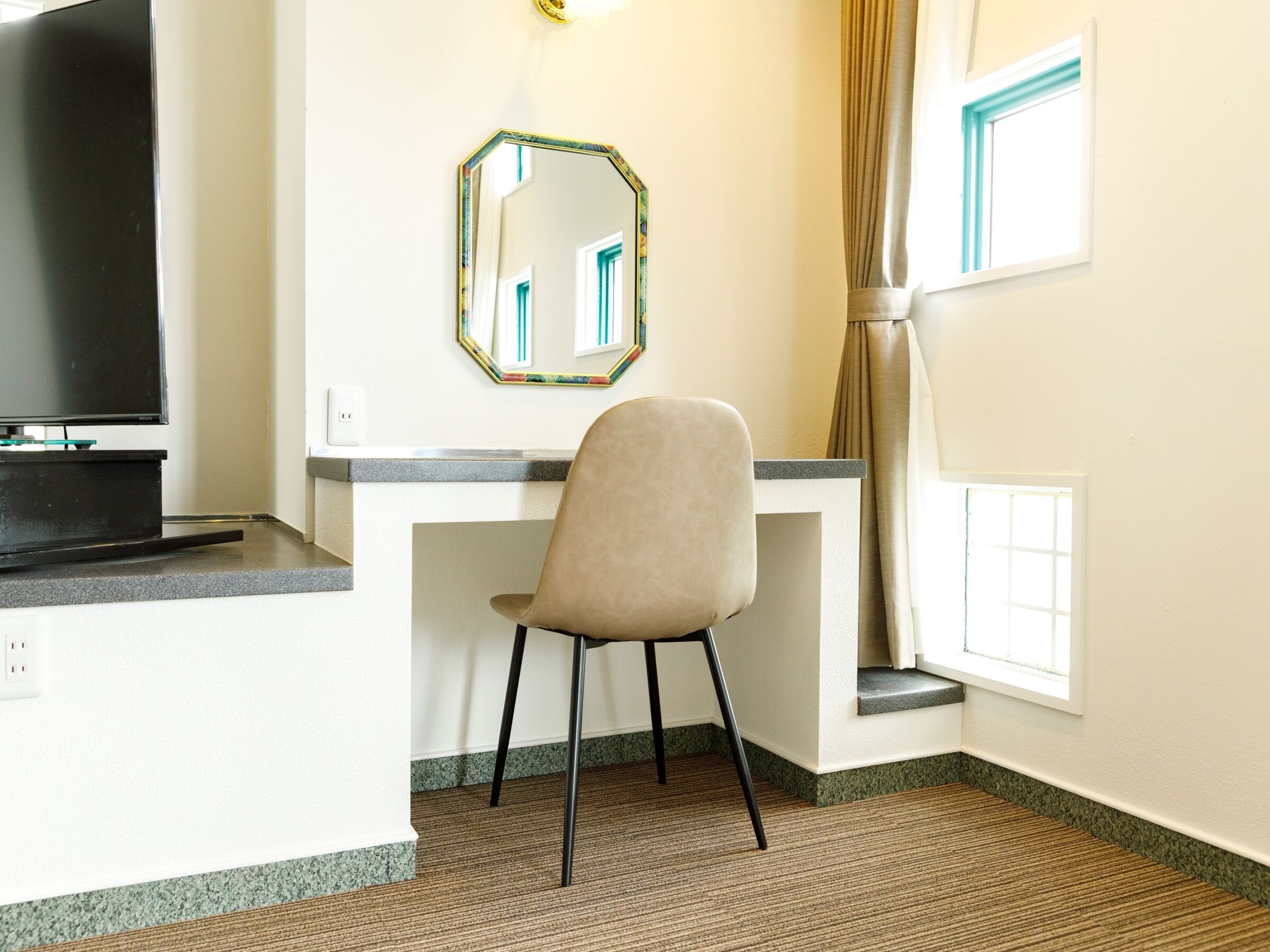 Une chambre d’hôtel équipée d’un bureau, d’une chaise, d’une télévision et d’une fenêtre avec des rideaux.