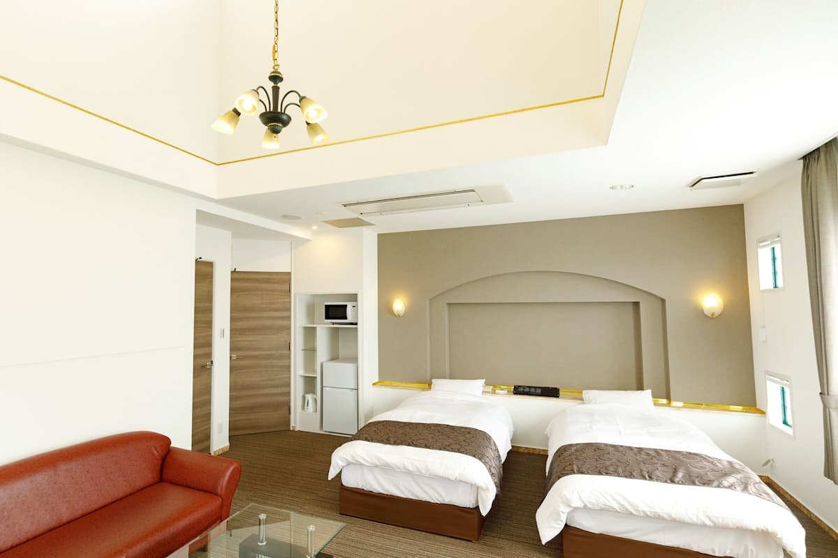 A hotel room with two beds, a red sofa, a glass coffee table, a microwave, and a TV.