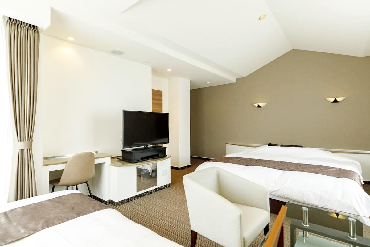 A hotel room with two beds, a TV on a stand, a desk, and a chair.