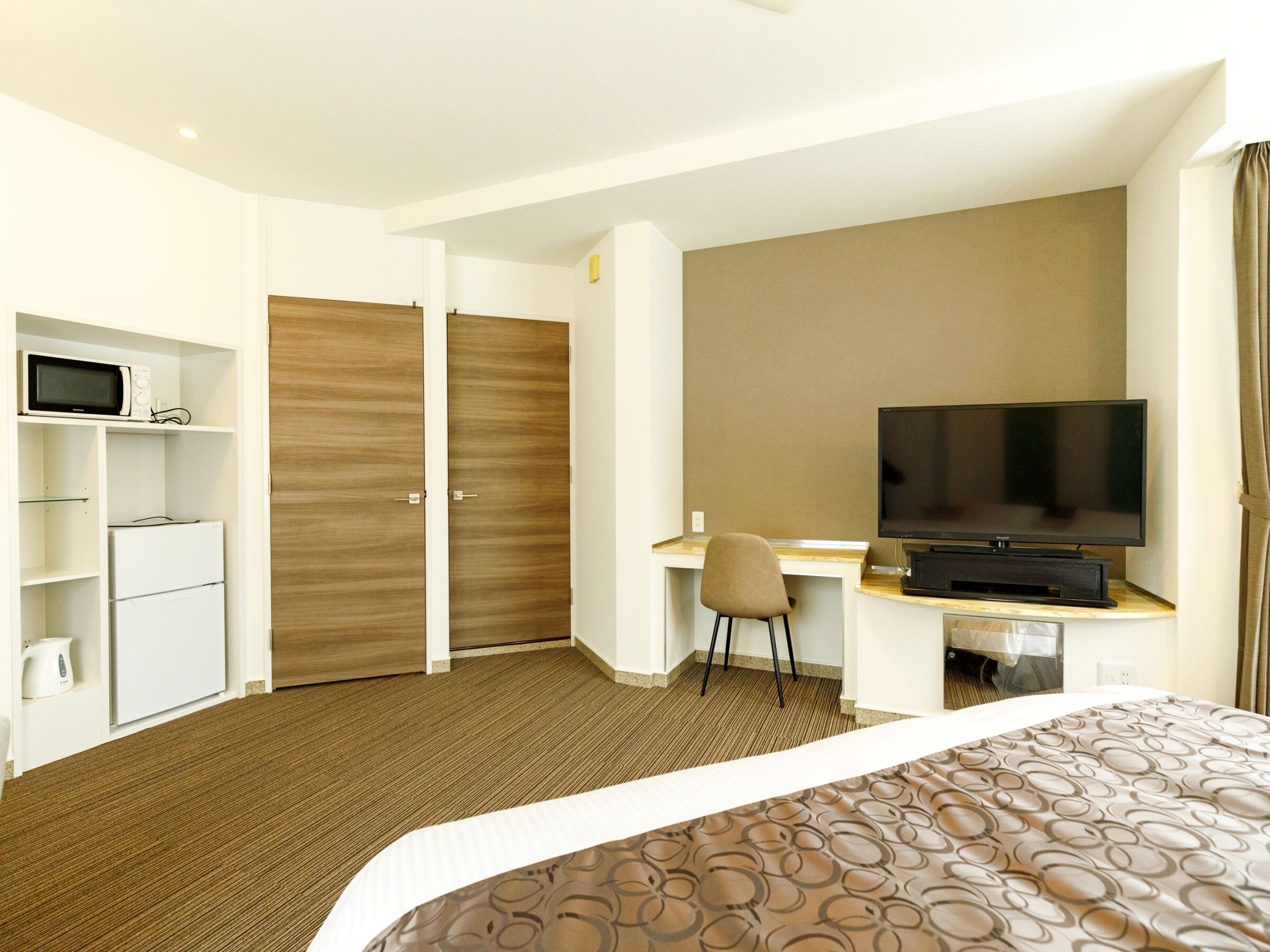A hotel room with a bed, a desk with a TV, a microwave, and a wardrobe.