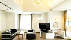A modern hotel room with a flat-screen TV, two black sofas, a small coffee table, a desk with a chair, and a large window with curtains. - BEPPU KANKO HOTEL ACE (Beppu)