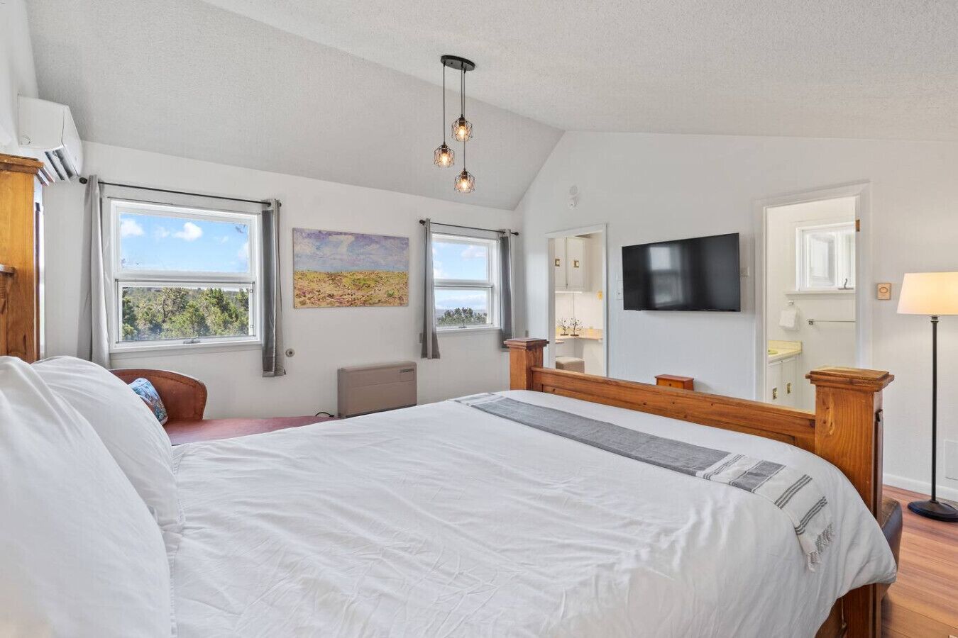 Une chambre à coucher avec un grand lit, une télévision, un tableau et une fenêtre donnant sur un beau paysage.