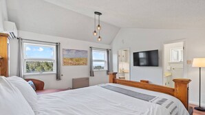 A bedroom with a large bed, a television, a painting, and a window with a view.