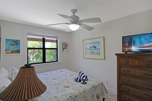 A bedroom with a bed, a ceiling fan, a window with blinds, a television on a wooden cabinet, and framed artwork on the wall. - Enjoy pool views from your Sanibel Island Villa - private beach - pet friendly - Signal Inn 04 (Sanibel)
