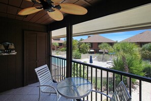 A covered balcony with a table and chairs, overlooking a pool and buildings. - Enjoy pool views from your Sanibel Island Villa - private beach - pet friendly - Signal Inn 04 (Sanibel)
