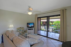 Ein Wohnzimmer mit Sofa, Fernseher, Deckenventilator und einer Schiebetür zu einer Terrasse.
