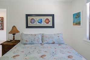 Un dormitorio con cama, mesita de noche, lámpara y cuadros en la pared.