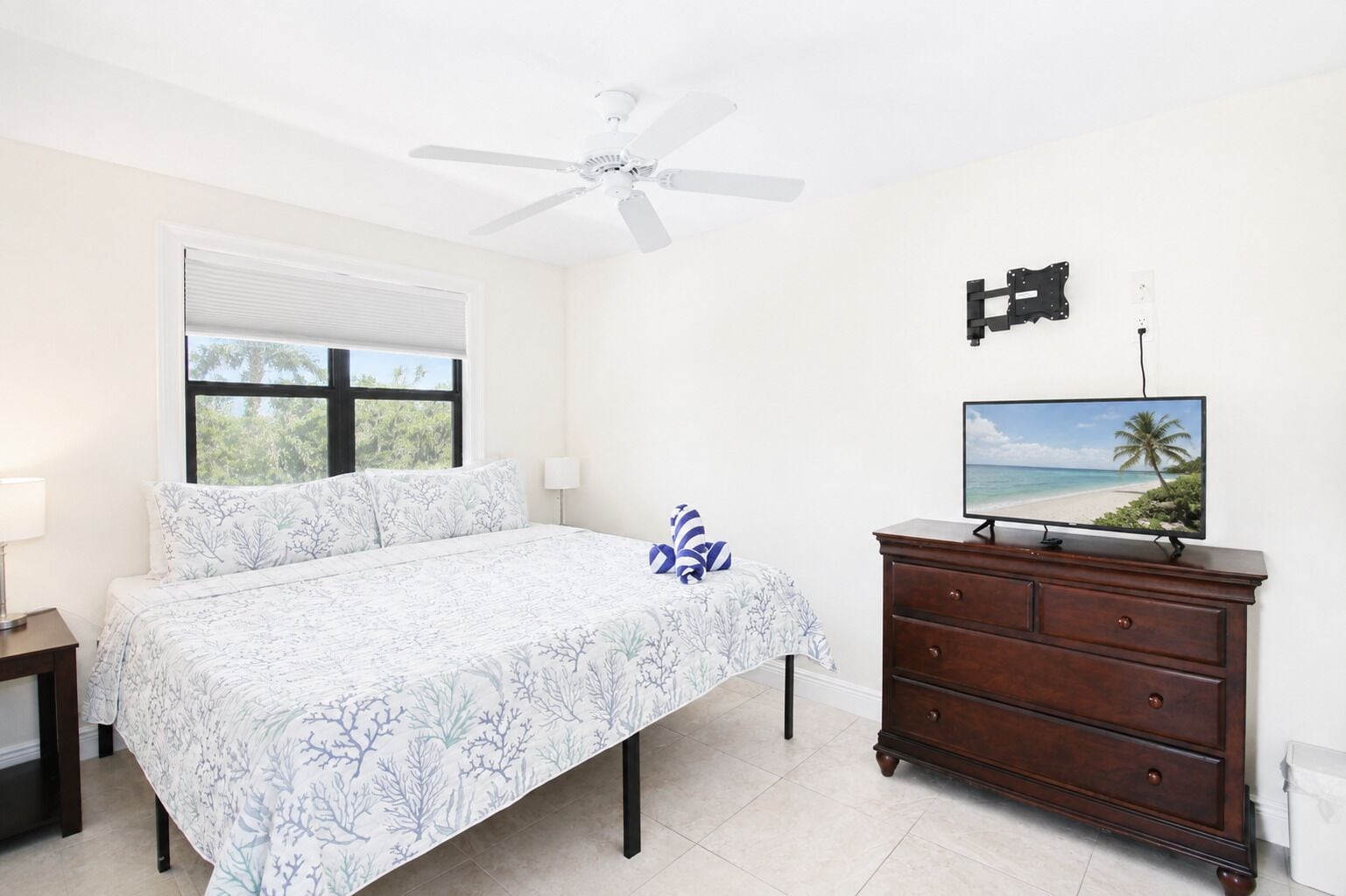 A bedroom with a bed, a nightstand, a dresser, a television, and a ceiling fan.
