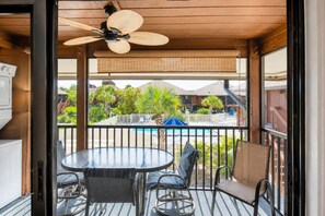 A balcony with a round table and chairs, a ceiling fan, and a view of a pool and buildings.