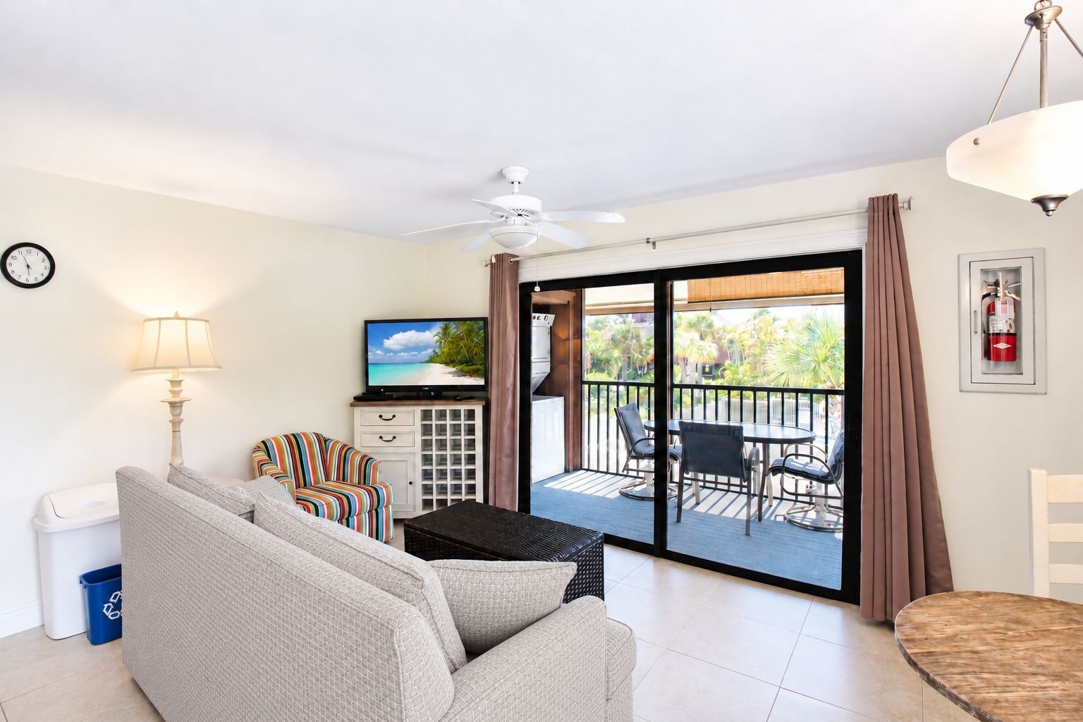 A living room with a sofa, TV, and a balcony with a table and chairs.