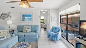Un salon avec un canapé bleu, un fauteuil à rayures, un ventilateur de plafond et de grandes fenêtres donnant sur la ville.