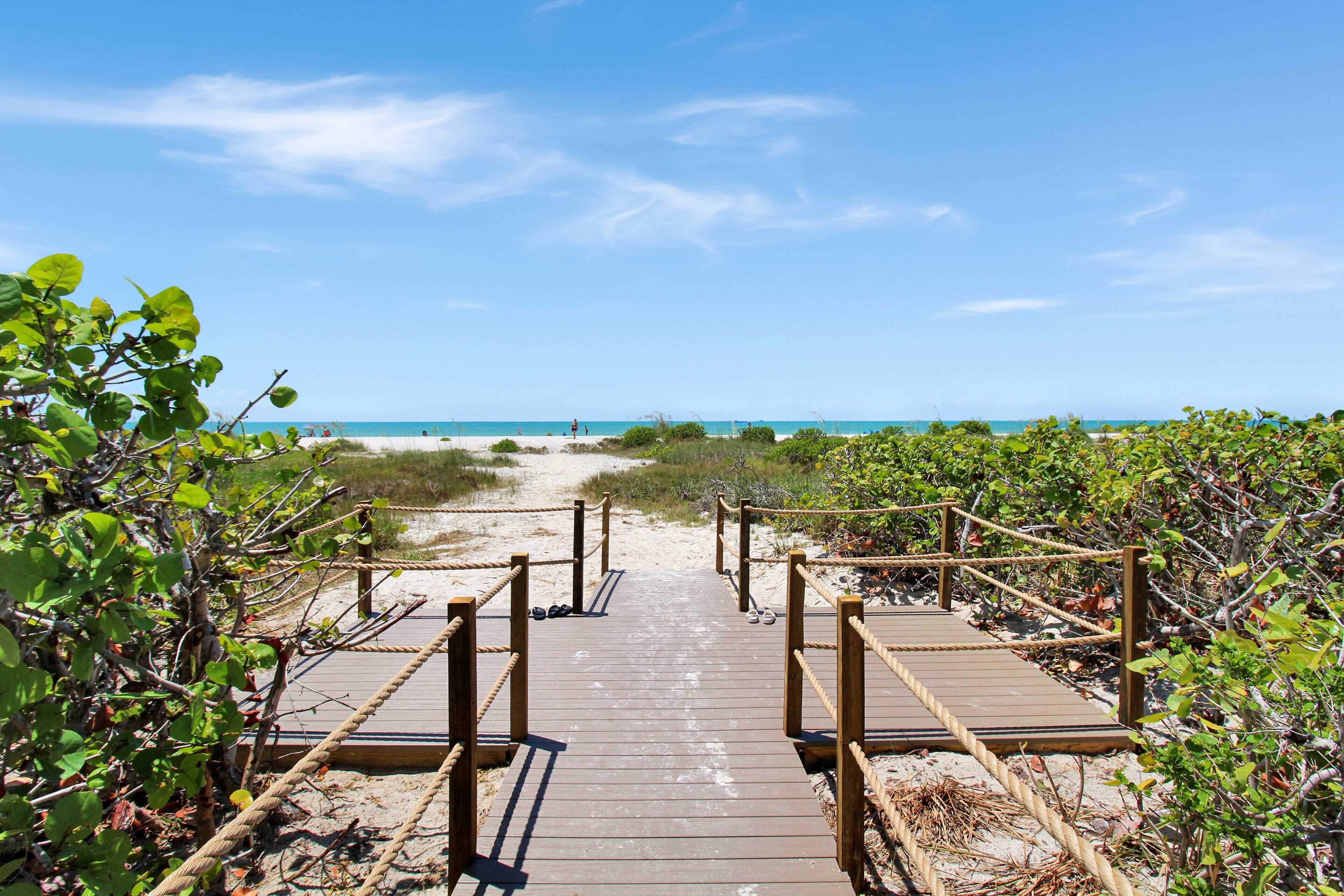 A wooden boardwalk leading to a beach with clear skies.