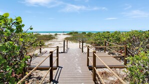 Une promenade en bois menant à une plage, avec un ciel dégagé.