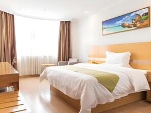 A hotel room with a large bed, a desk, a chair, and a painting of a beach scene on the wall. - Greentree Alliance Hotel Foshan Nanhai District Pingzhou Yuqi Street (Foshan)