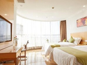 A hotel room with two beds, a desk, a TV, and a large window with curtains.