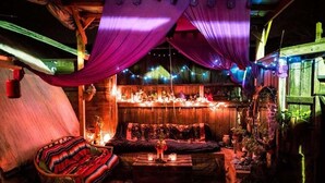Um quarto acolhedor, com iluminação suave e interior rústico em madeira, um banco estofado e uma pequena mesa com velas.