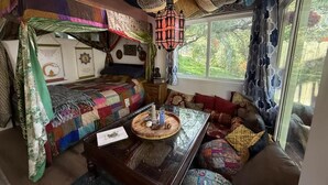 Um quarto aconchegante com uma janela grande, uma mesa de centro de madeira e um edredom colorido com patchwork.
