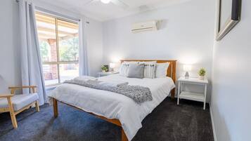 A bedroom with a bed, a chair, a bedside table, a nightstand, a ceiling fan, and an air conditioning unit.