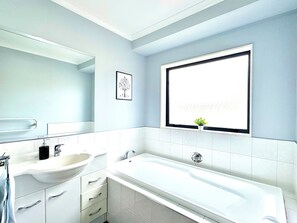 A modern bathroom with a large bathtub, a sink with a mirror, and a window with a view.