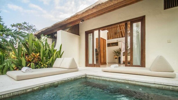 A poolside area with a clear pool, two lounge chairs, and a thatched roof structure. - Kembali On The River by Balipras (Cepaka)