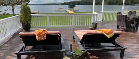 A deck with two lounge chairs, a pergola, and a view of a lake.