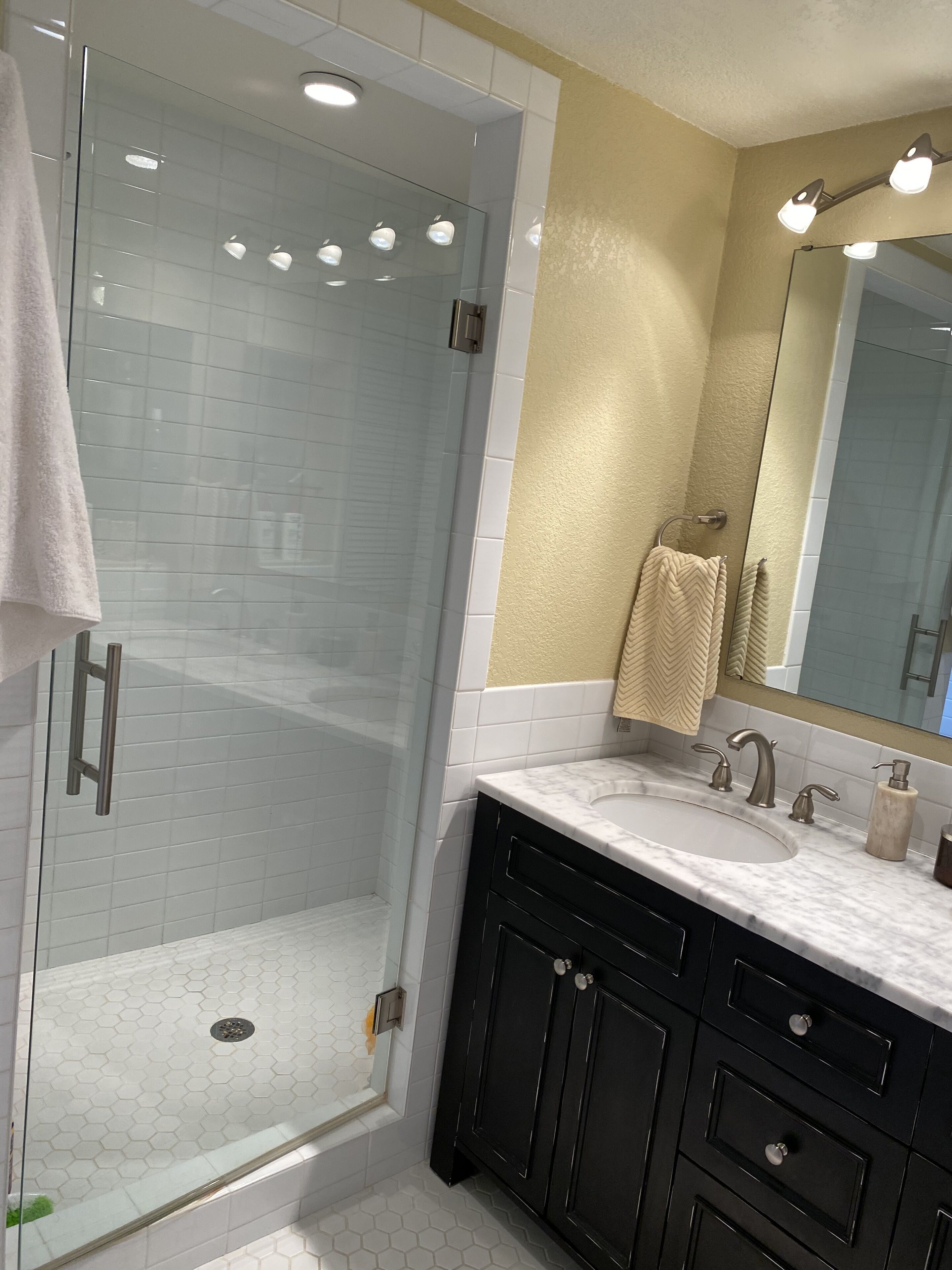 A modern bathroom with a glass-enclosed shower, a vanity with a sink, and a large mirror.