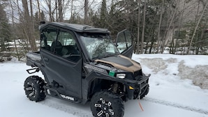 Een Polaris 1000 sneeuwscooter geparkeerd in een besneeuwd gebied met bomen op de achtergrond.