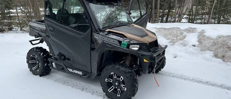 A Polaris 1000 snowmobile parked in a snowy area with trees in the background.