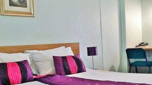 Una habitació d'hotel amb un llit, un escriptori amb una cadira i una làmpada.