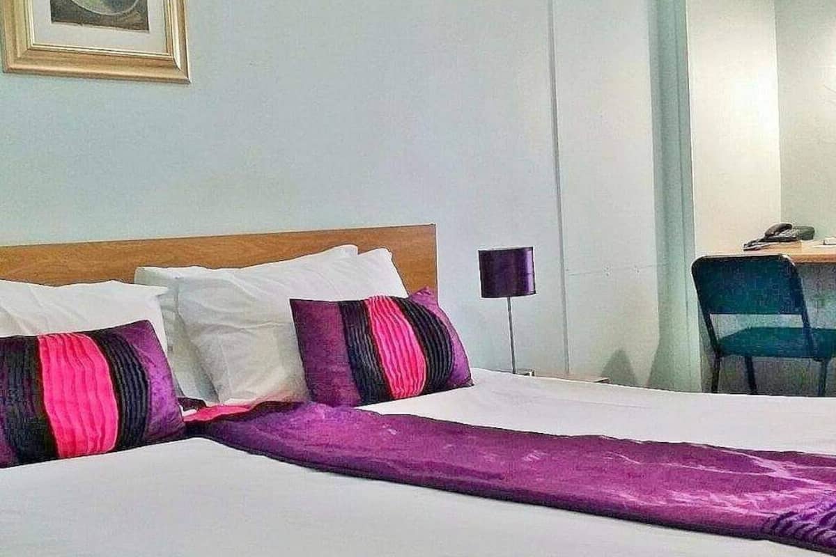 Hotellihuone, jossa on sänky, työpöytä tuolilla ja lamppu.