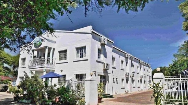 Edifici blanc amb nombroses finestres i balcons, envoltat de plantes en testos i un portal reixa.