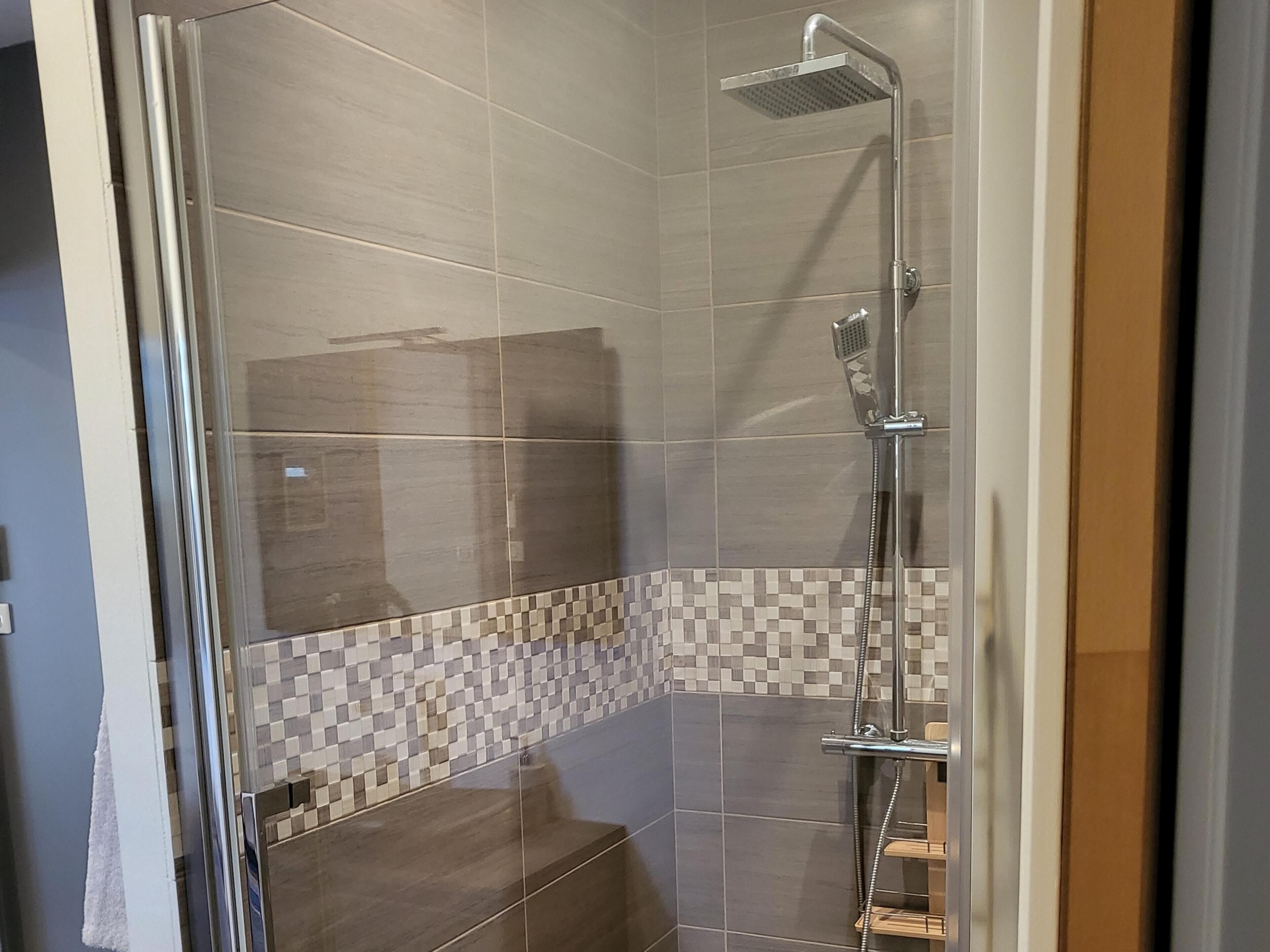 A shower with a glass door, tiled walls, and a checkered tile pattern at the base.