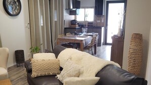 Een woonkamer met een donker leren bank, een houten salontafel en een eethoek op de achtergrond.
