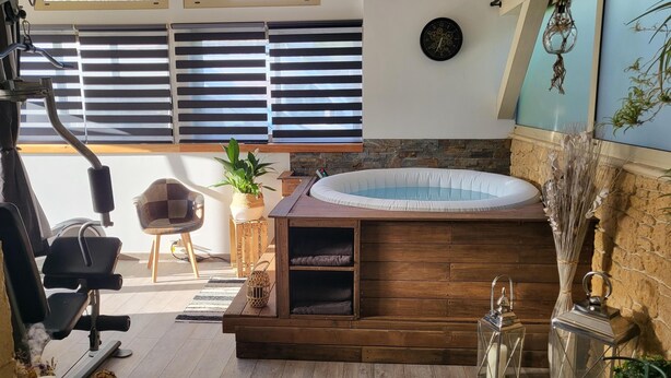 Een moderne spa met een houten jacuzzi, fitnessapparatuur en een stenen muur.