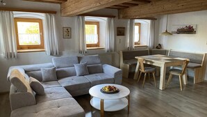 A cozy living room with a sectional sofa, a round coffee table, a wooden dining table with chairs, and a bench. - Apartment 'Haus Peschl Fewo 1' with Shared Terrace, Shared Garden and Wi-Fi (Neureichenau)