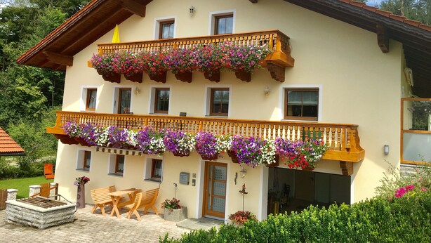 A two-story building with balconies adorned with flower boxes, a wooden bench, and a stone fireplace. - Apartment 'Haus Peschl Fewo 1' with Shared Terrace, Shared Garden and Wi-Fi (Neureichenau)