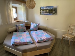 A bedroom with a bed, two pillows, a chair, a lamp, a painting, and a window with curtains. - Apartment 'Haus Peschl Fewo 1' with Shared Terrace, Shared Garden and Wi-Fi (Neureichenau)